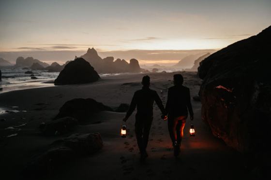 Couple carrying lanterns along a beach at sunset